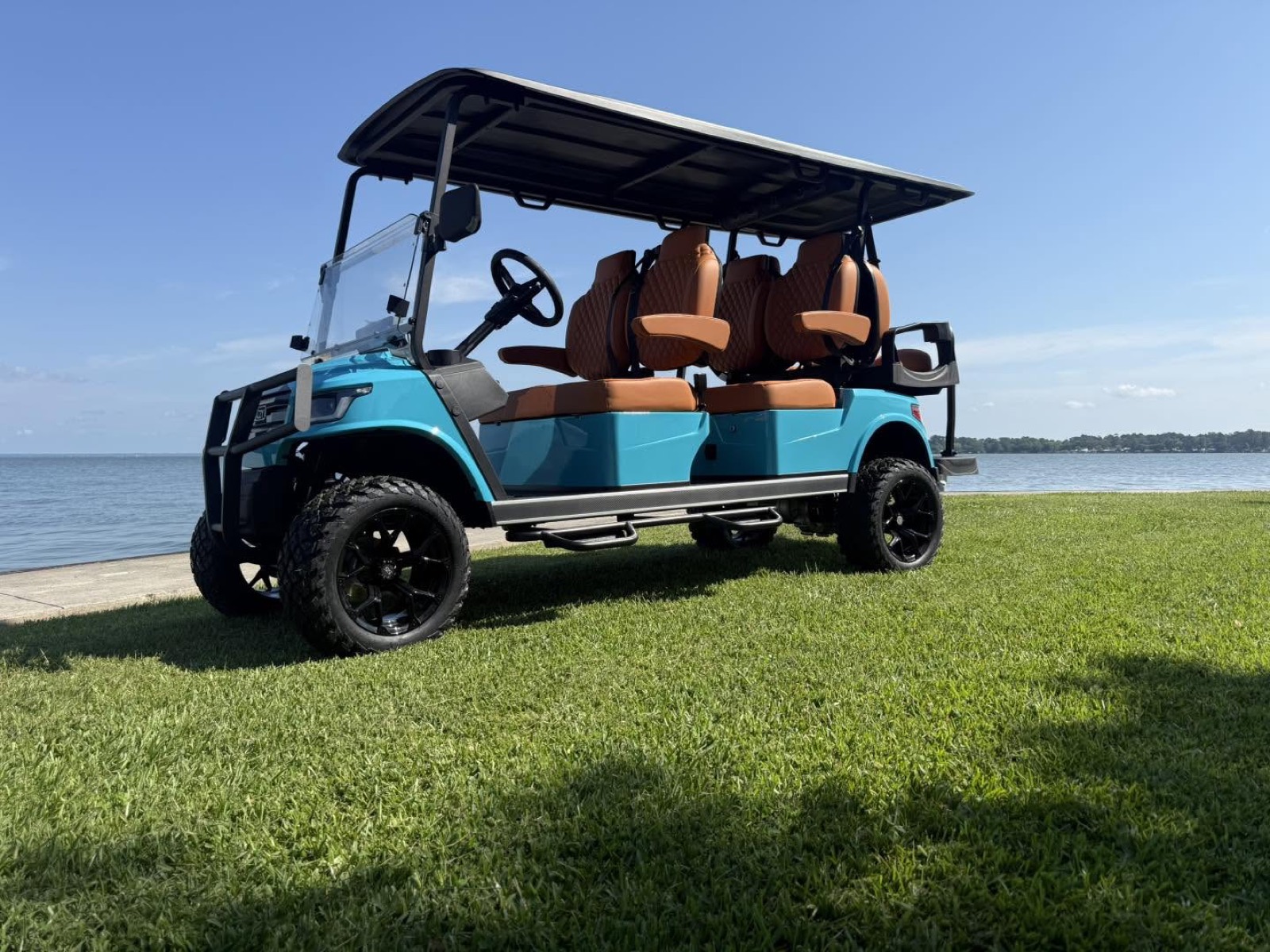 Teal 6-seater Breezy EV golf cart with lifted off-road tires beside East Texas lake