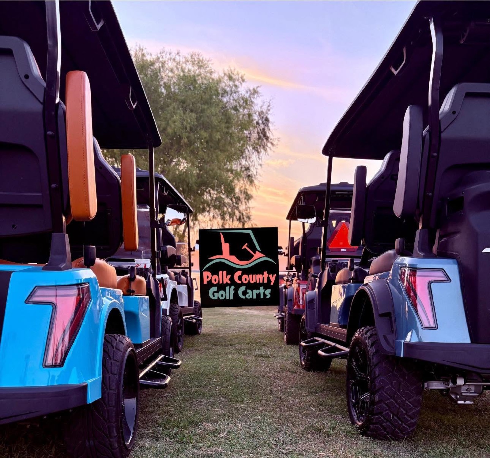 Two lifted Breezy EV carts photographed at sunset with the PCGC sign between them